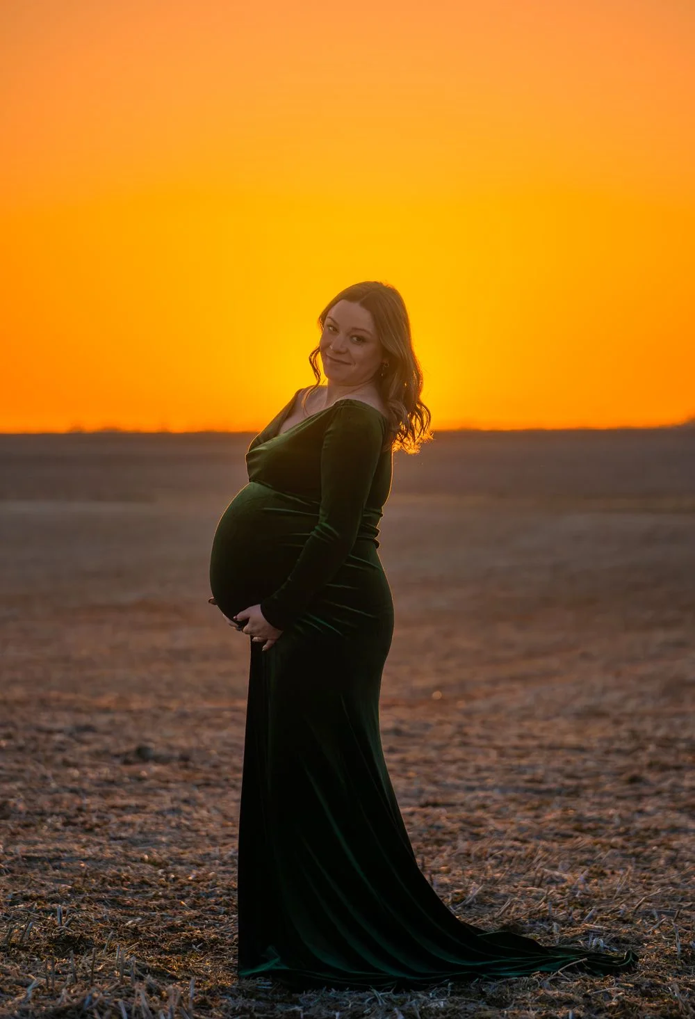 Maternity portrait in a green gown at sunset.