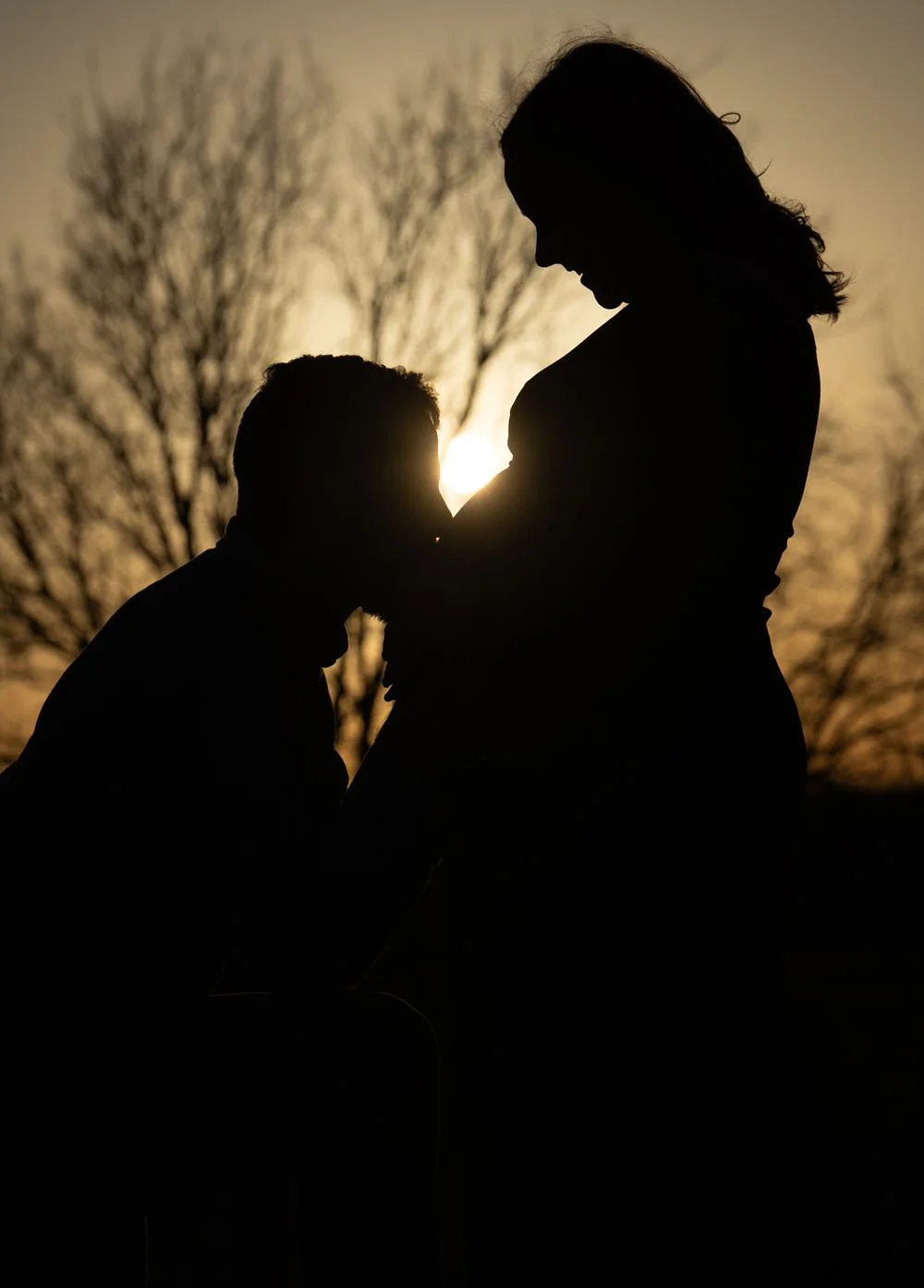 Silhouette of an expecting couple against an orange sunset.